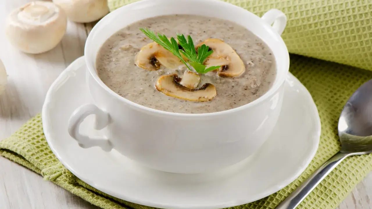 Un réconfortant velouté de champignon, garni de lamelles et d'une touche de persil, servi dans une tasse blanche sur une serviette verte.