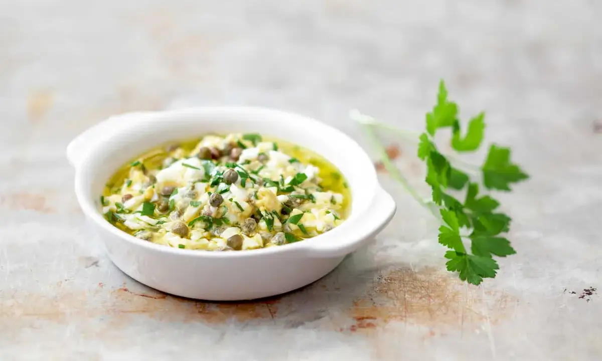 Un bol de sauce gribiche, garnie de persil frais et de câpres, prête à accompagner un plat.