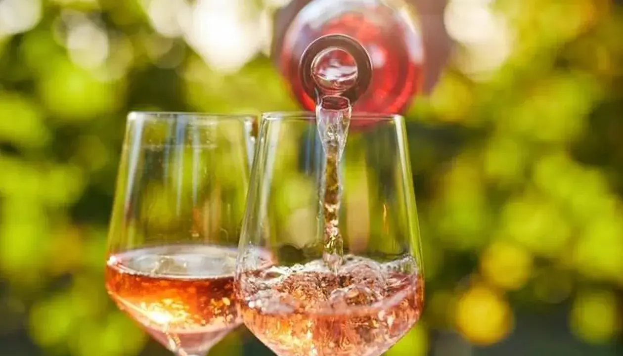 Le danger du vin rosé : une bouteille verse son contenu dans deux verres, créant une cascade pétillante sous un soleil radieux.