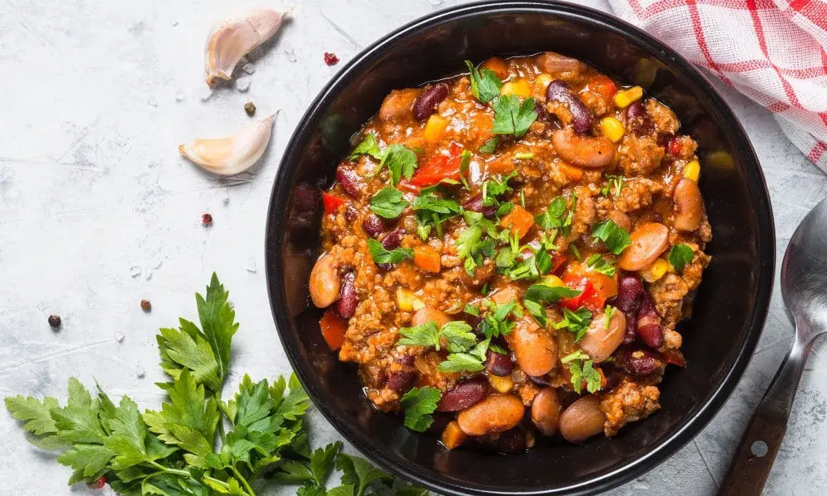 Un bol de chili sin carne, garni de persil frais. Des haricots rouges, du maïs et des dés de poivrons se mêlent à la viande hachée dans cette recette réconfortante.