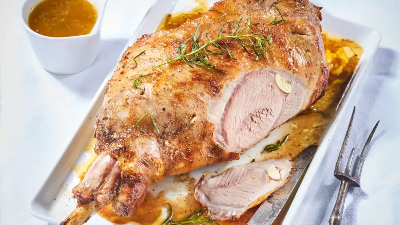 Un gigot d'agneau rôti, doré et juteux, garni de romarin et d'ail, servi avec sa sauce. Un délice à partager.