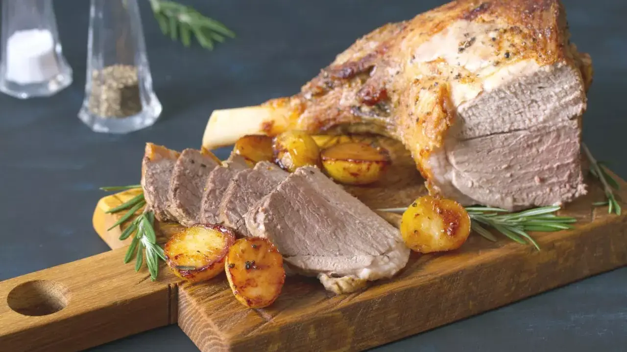 Un gigot de 7 heures, tendre et savoureux, servi avec des pommes de terre rôties et du romarin sur une planche en bois.