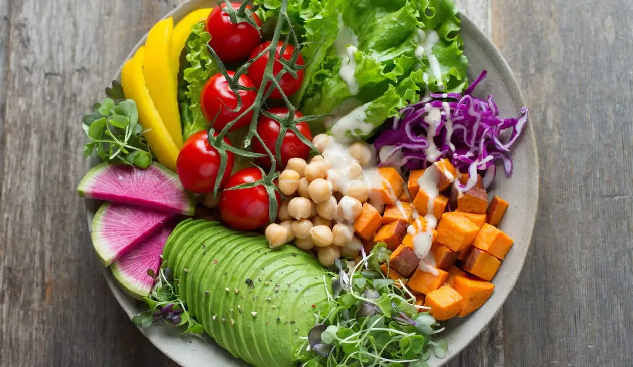 Une assiette colorée avec avocat, tomates, pois chiches, patates douces, chou rouge, radis et poivron jaune. Une belle idée de salade composée.