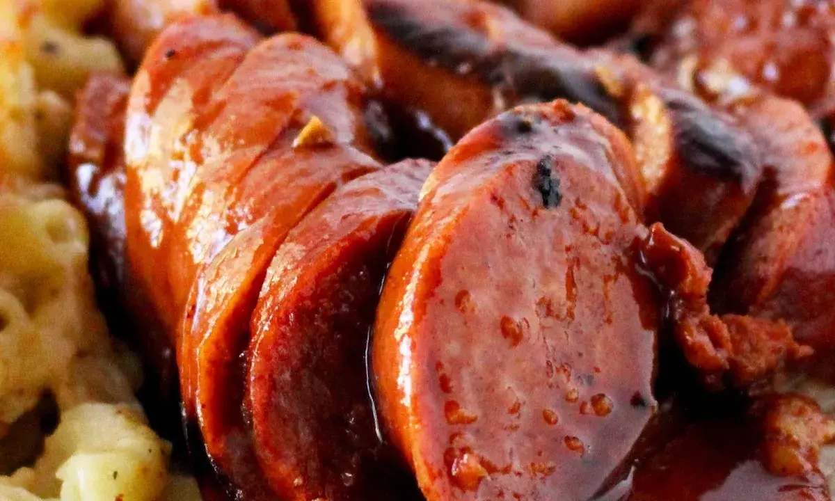 Rougail saucisse, un plat réunionnais savoureux avec des saucisses coupées en rondelles, nappées d'une sauce brune et accompagnées de pâtes.