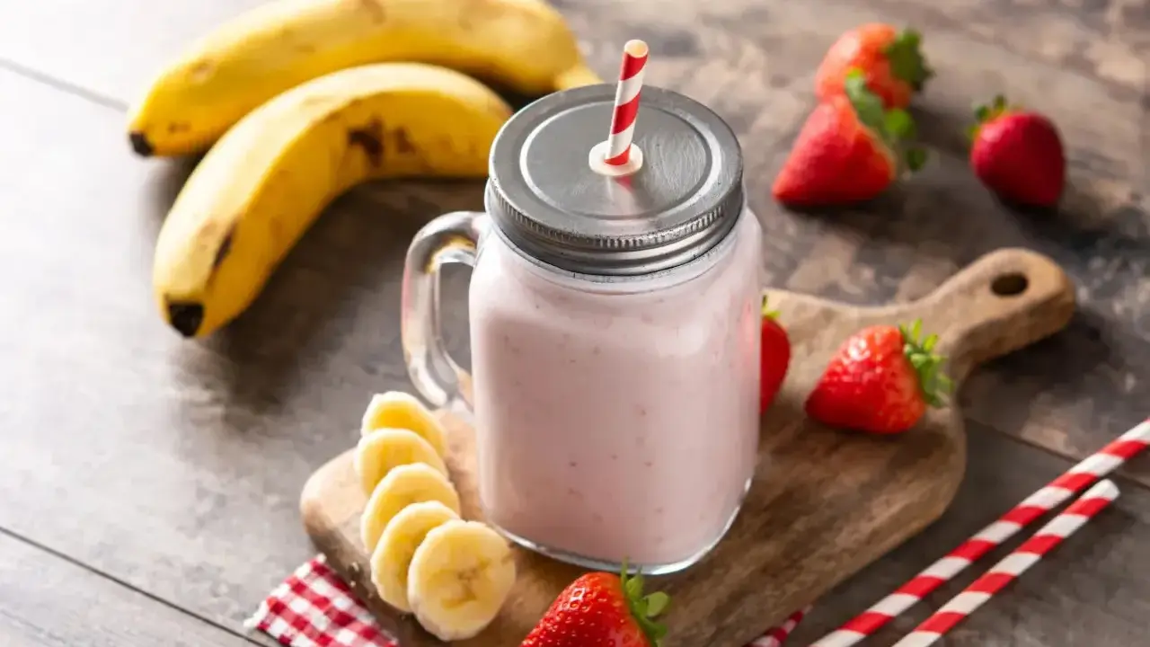 Un délicieux smoothie fraise banane dans un bocal en verre, garni de fruits frais et de pailles rayées.