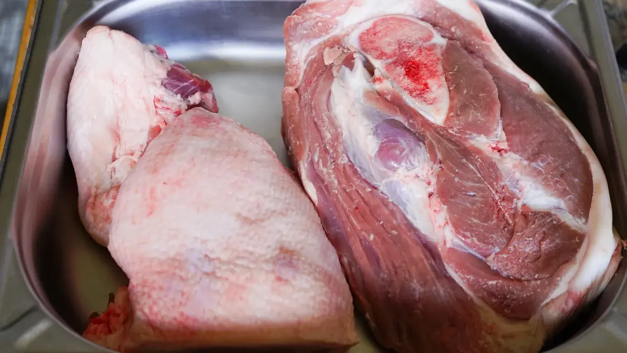 Deux morceaux de viande crue, dont une belle rouelle de porc, reposent dans un bac en métal.