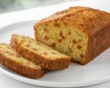 Tranche de cake salé au chorizo, parsemé de petits morceaux rouges et de fines herbes vertes.