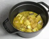 Un plat mijoté de colombo de porc avec des morceaux de pommes de terre et des épices dans une cocotte en fonte noire.