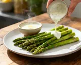Une sauce hollandaise au siphon est versée sur des asperges vertes sur une assiette.