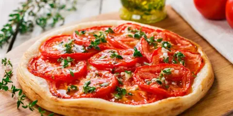 Tarte aux tomates cerises, garnie d'herbes fraîches et d'ail, prête à être dégustée.