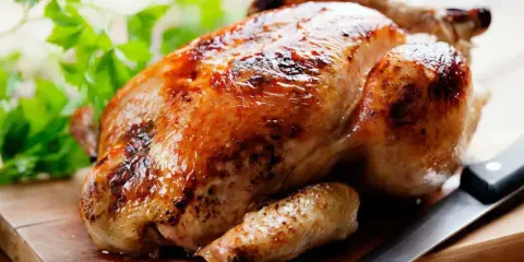 Un appétissant poulet rôti sur une planche en bois, prêt à être dégusté. Quel vin avec poulet rôti ? Un blanc fruité ou un rouge léger serait parfait.