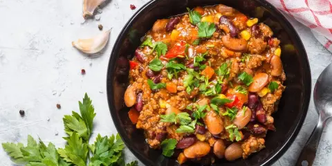 Un bol de chili sin carne, garni de persil frais. Des haricots rouges, du maïs et des dés de poivrons se mêlent à la viande hachée dans cette recette réconfortante.