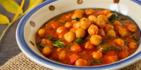 Un savoureux curry de pois chiche, aux couleurs chaudes, servi dans un bol décoré. Une touche de verdure et des feuilles jaunes apportent une note automnale.