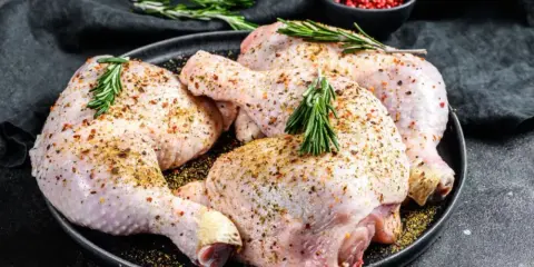Quatre cuisses de poulet crues, assaisonnées et garnies de romarin, prêtes pour une marinade poulet savoureuse.