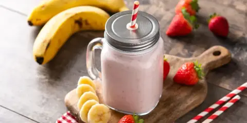 Un délicieux smoothie fraise banane dans un bocal en verre, garni de fruits frais et de pailles rayées.