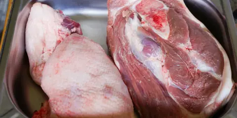 Deux morceaux de viande crue, dont une belle rouelle de porc, reposent dans un bac en métal.