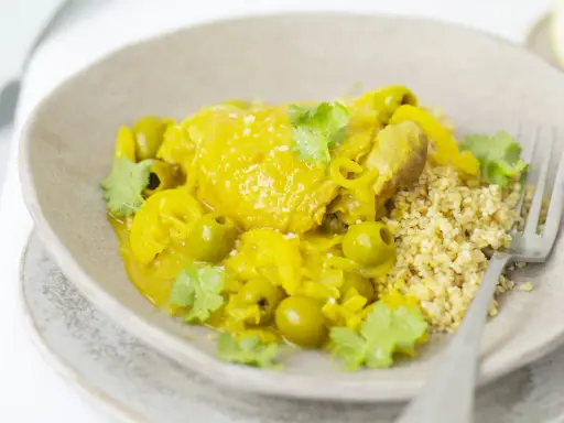 Un plat de tajine poulet citron, parfumé et coloré, servi avec du couscous et des olives vertes.