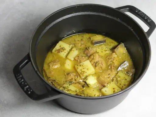Un plat mijoté de colombo de porc avec des morceaux de pommes de terre et des épices dans une cocotte en fonte noire.
