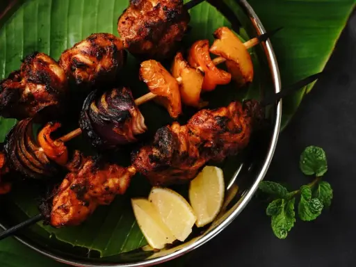 Brochettes de poulet grillées, marinées et savoureuses, avec oignons et poivrons, servies sur une feuille de bananier avec des quartiers de citron.