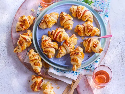 Petits croissants au jambon dorés, certains saupoudrés de graines de sésame ou de pavot, prêts à être dégustés.