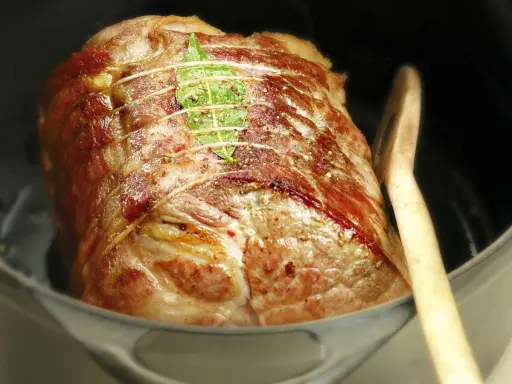 Un rôti de porc cocotte, doré et savoureux, est prêt à être dégusté. Une feuille de laurier orne sa surface.