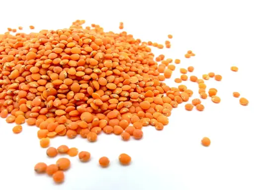 Un tas de lentilles corail, petites et orangées, s'étale sur un fond blanc. Elles sont prêtes à être cuisinées.