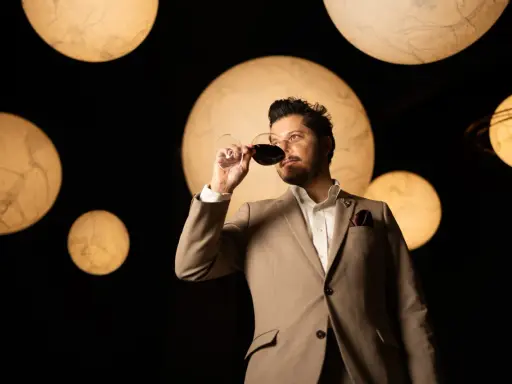 Un homme en costume déguste un verre de vin rouge, entouré de lumières rondes évoquant des planètes. Une dégustation qui rappelle la philosophie du vin biodynamique.