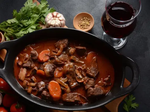 Un plat de vin avec bœuf bourguignon mijoté, garni de carottes et champignons, accompagné d'un verre de vin rouge.