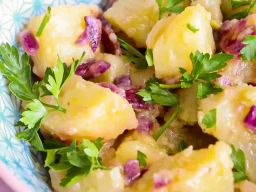 Salade de pomme de terre crémeuse avec des oignons rouges et du persil frais, servie dans un bol décoratif.
