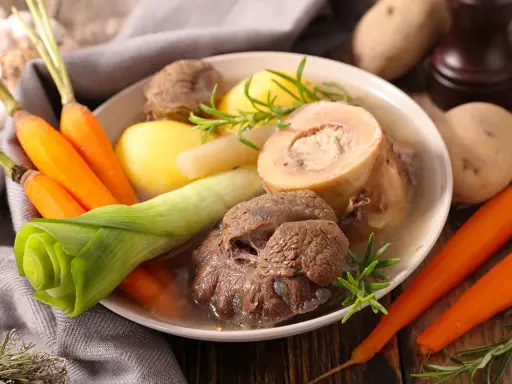 Un plat réconfortant de pot au feu, avec du bœuf, des carottes, des pommes de terre et des poireaux, garni de romarin.
