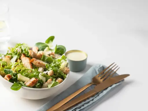 Salade César fraîche avec poulet grillé, croûtons et copeaux de parmesan, accompagnée de sa sauce crémeuse.