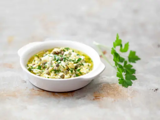 Un bol de sauce gribiche, garnie de persil frais et de câpres, prête à accompagner un plat.