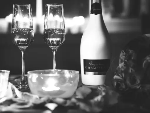 Deux flûtes de champagne pétillant, une bouteille de "Besgane bianc CHAMPAGNE" et des roses, ambiance romantique.