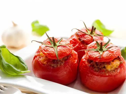 Trois tomates farcies au four, garnies d'une farce savoureuse, servies avec des feuilles de basilic frais.