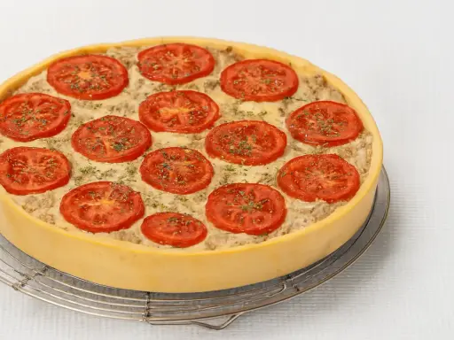 Une délicieuse quiche au thon, garnie de rondelles de tomates fraîches et d'herbes, prête à être dégustée.