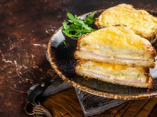 Deux croque monsieur bechamel dorés, garnis de jambon et de fromage fondant, servis avec une salade verte.