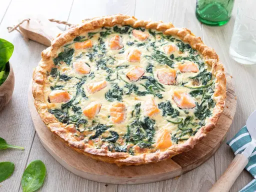 Une délicieuse quiche saumon épinard, dorée et garnie de morceaux de poisson et de légumes verts, prête à être dégustée.