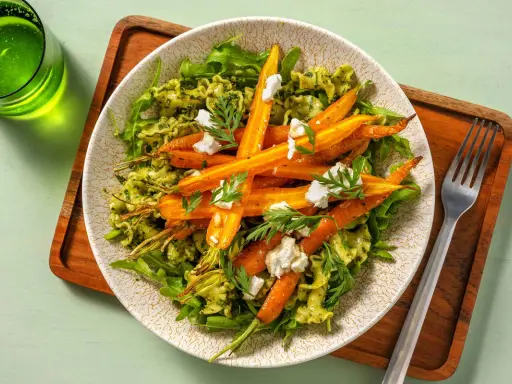 Pâtes vertes avec des carottes rôties et du fromage émietté, garnies de fanes de carottes fraîches.