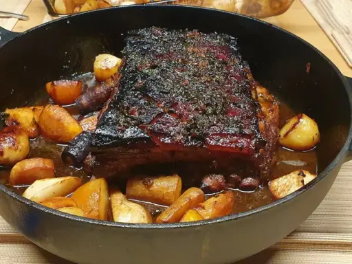 Poitrine de porc rôtie, croustillante et savoureuse, servie avec des pommes de terre et des carottes dans une cocotte en fonte.