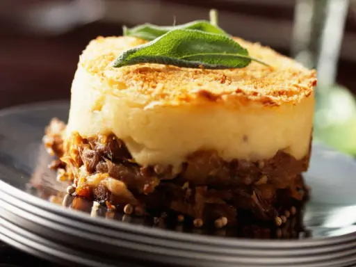 Un délicieux parmentier de canard, gratiné et garni d'une feuille de sauge, servi sur une assiette élégante.