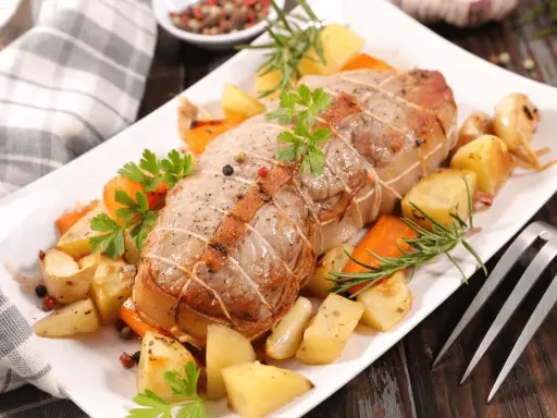 Rôti de veau savoureux, entouré de pommes de terre rôties, carottes et herbes aromatiques, prêt à être dégusté.