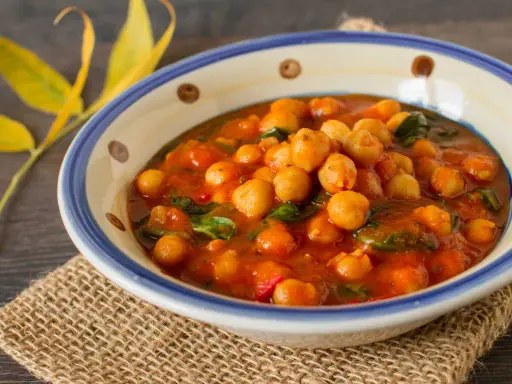 Un savoureux curry de pois chiche, aux couleurs chaudes, servi dans un bol décoré. Une touche de verdure et des feuilles jaunes apportent une note automnale.