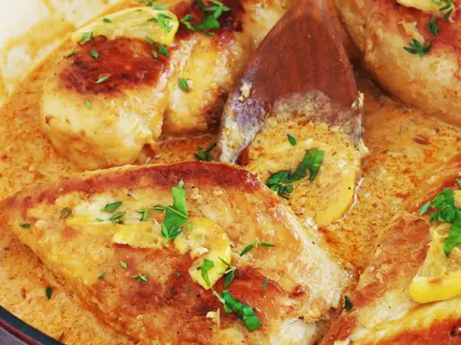 Un délicieux poulet à la crème, garni de persil frais et de rondelles de citron, mijote dans une sauce onctueuse.