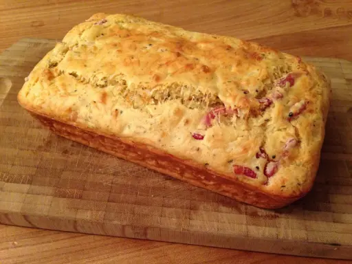 Un délicieux cake aux lardons, doré et moelleux, prêt à être dégusté sur une planche en bois.