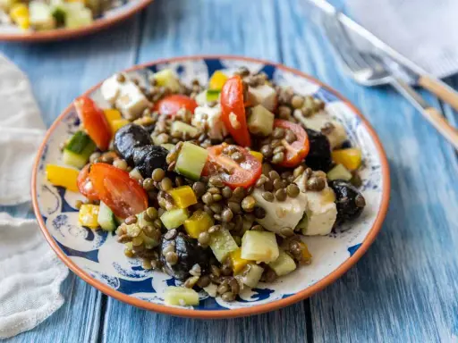 Salade colorée de lentilles vertes avec tomates, concombre, olives noires et feta. Un plat frais et savoureux.