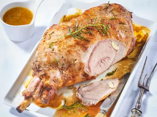Un gigot d'agneau rôti, doré et juteux, garni de romarin et d'ail, servi avec sa sauce. Un délice à partager.