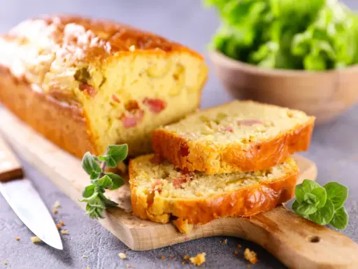 Tranche de cake jambon fromage dorée, garnie d'herbes fraîches, prête à être dégustée.