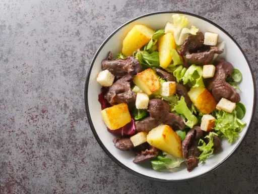 Salade de gésiers savoureuse avec pommes de terre rôties, croûtons et salade verte fraîche. Un délice pour les amateurs de cuisine française.