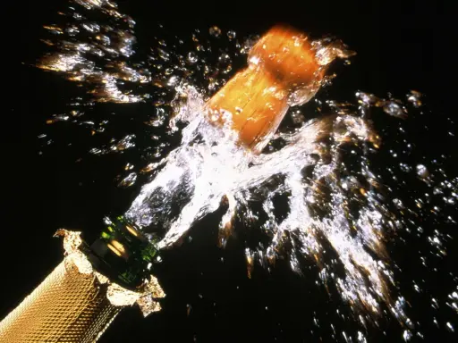 Le bouchon d'une bouteille de champagne s'envole dans un jet d'eau et de bulles, un moment de joie pour sabler le champagne.