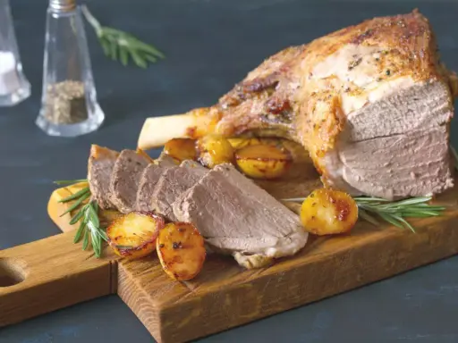 Un gigot de 7 heures, tendre et savoureux, servi avec des pommes de terre rôties et du romarin sur une planche en bois.